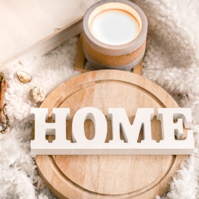 Cozy home decor items with wooden letters, candle and book on the background of beautiful white plaid, home atmosphere concept